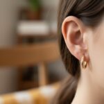A close-up of gold huggie earrings with a hinged closure worn on an ear
